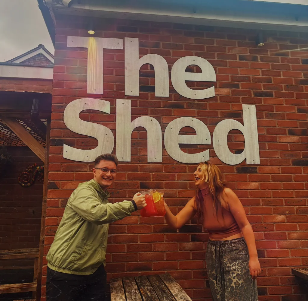 Friends toasting in front of The Shed sign