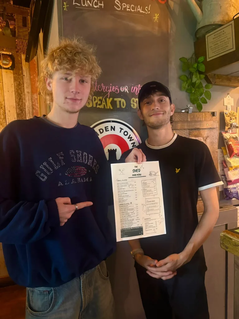 Two members of The Shed team holding a menu